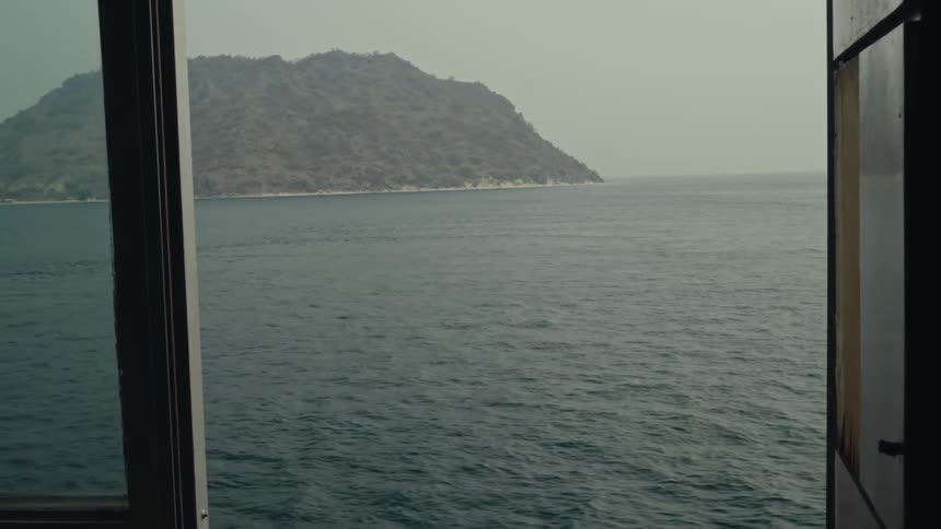 A view of the ocean and a distant island is seen through the open window of a boat