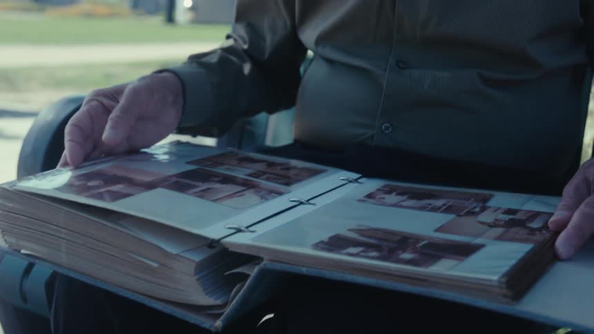 Man sitting outside on a park bench looking at a photo album