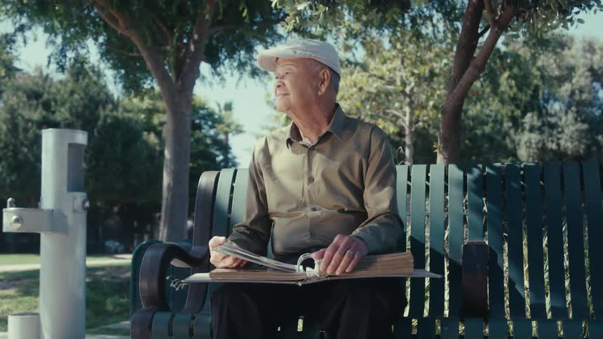 Elderly man sitting on a bench in the park outdoors with a photo album
