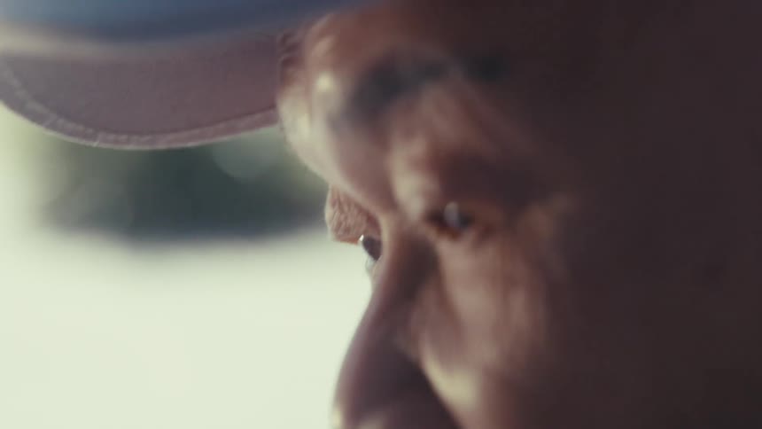 Close up of the face of an elderly man wearing a baseball cap and talking