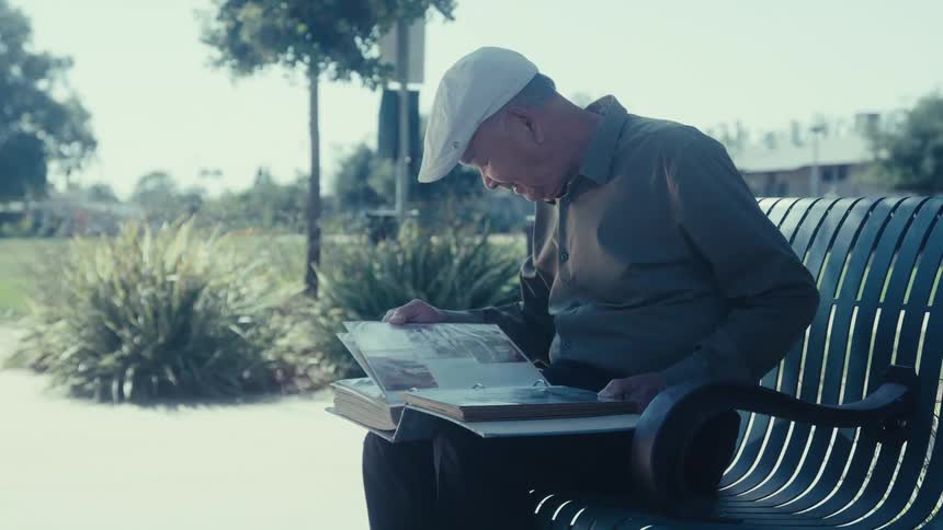 Elderly man sitting on a bench outdoors and looking at a photo album