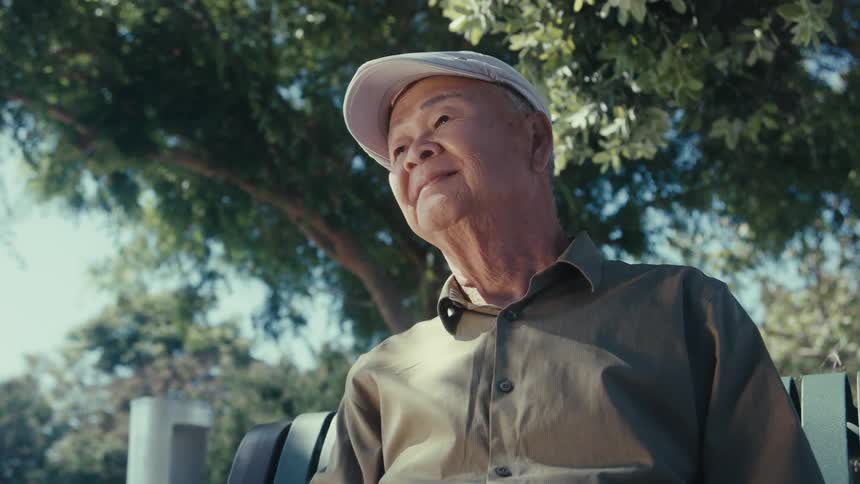 Elderly man is smiling and sitting on a park bench