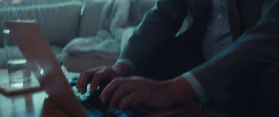 A man in a business suit types on a laptop at home