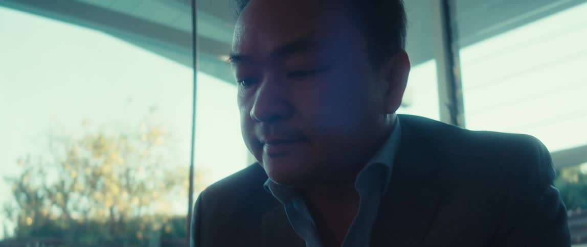 A person in a suit is typing on a silver apple laptop placed on a wooden table with a glass of water nearby