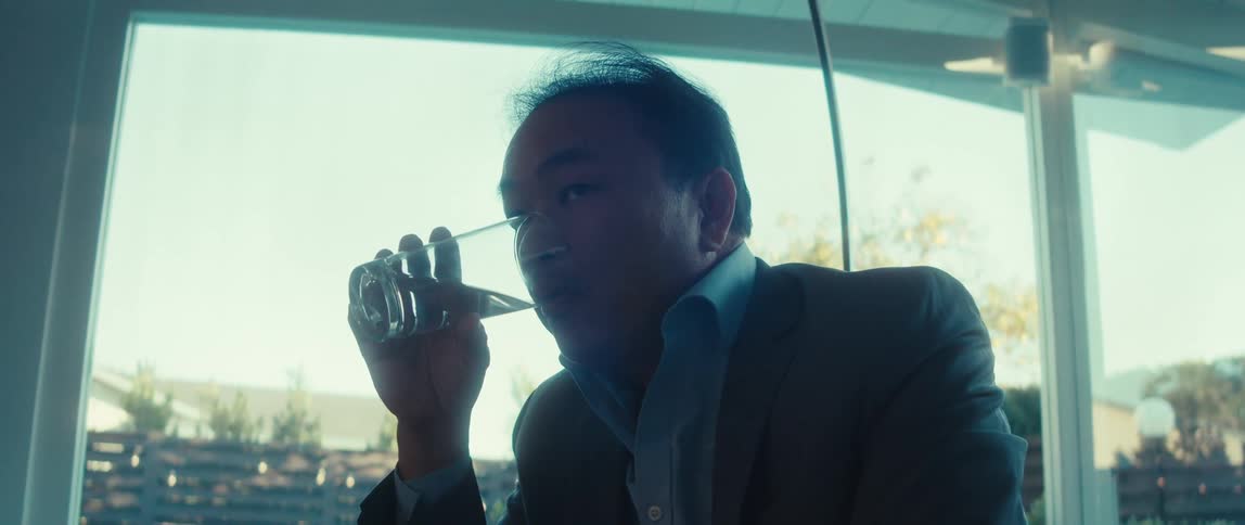 An asian man drinks water out of a glass