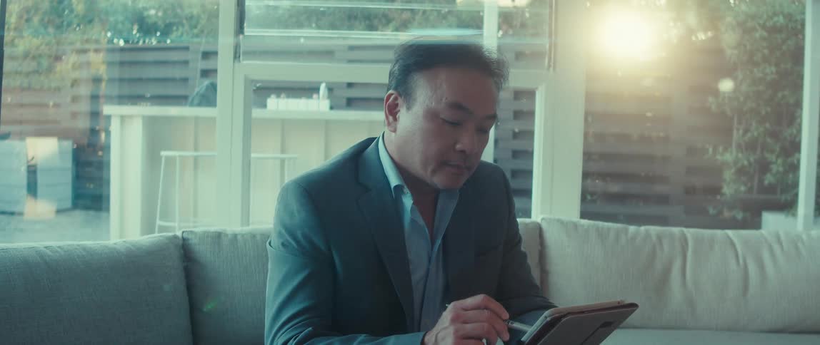 A man in a business suit sits at home on a sunny morning using a tablet