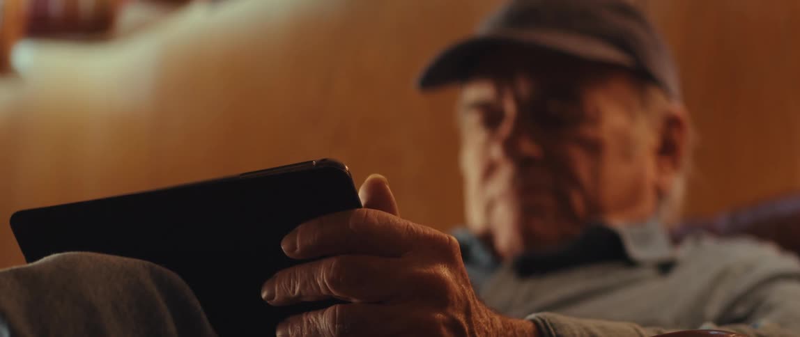 Elderly man is sitting inside his home and looking at a tablet