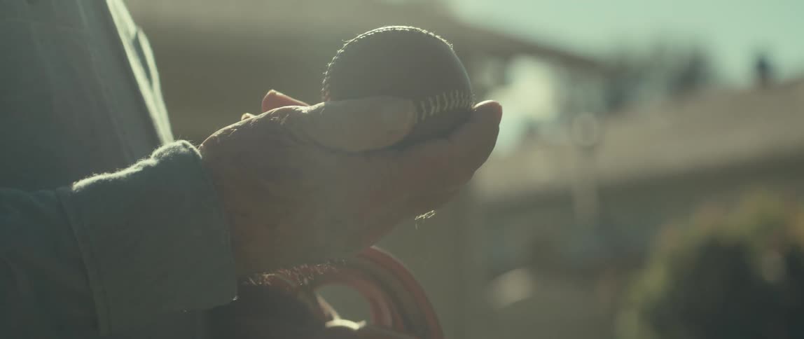 An elderly man holds a vintage baseball in his hands on a sunny day