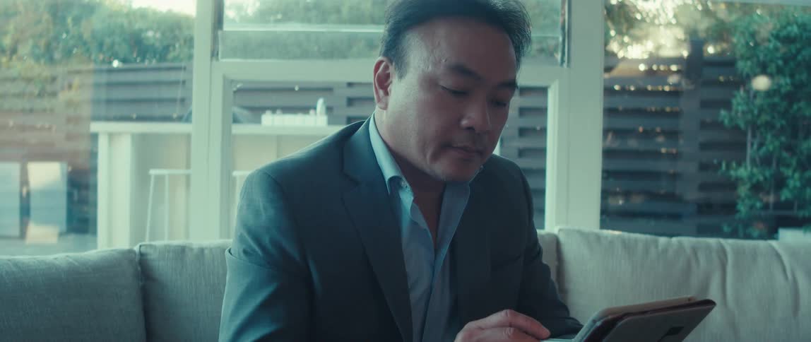 A man in a suit uses a tablet as sunlight streams through the windows