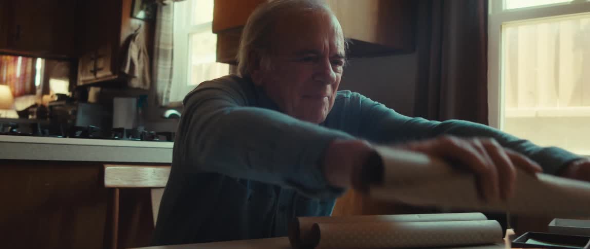 Smiling old man prepares to wrap a box in brown wrapping paper