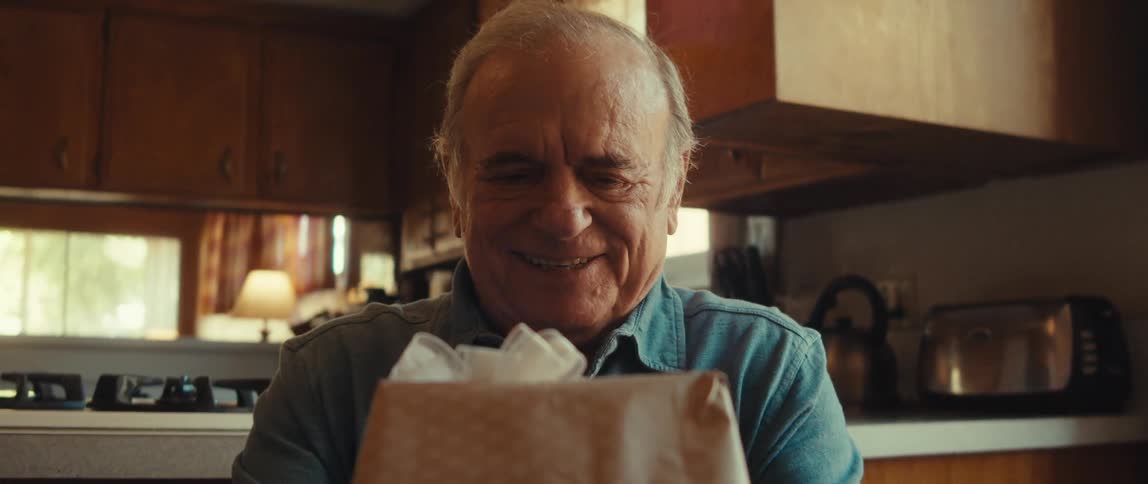 A cheerful elderly man is holding a gift box in a cozy room at home