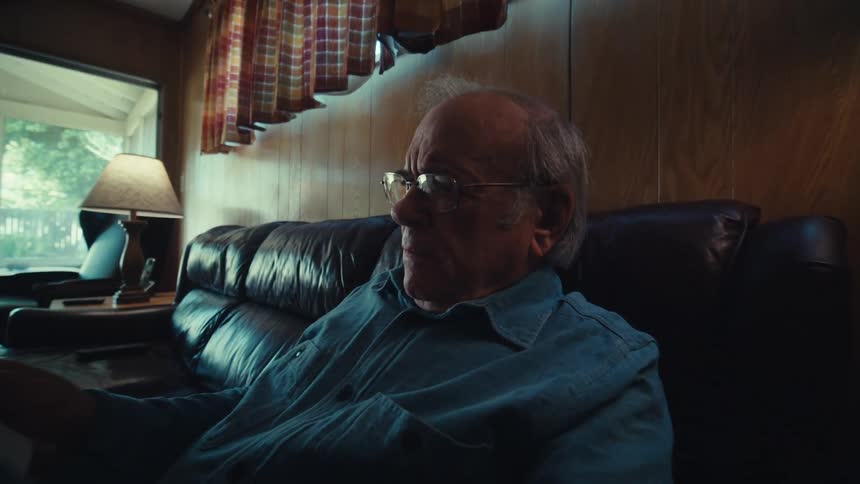 Elderly man sitting in living room reading newspaper