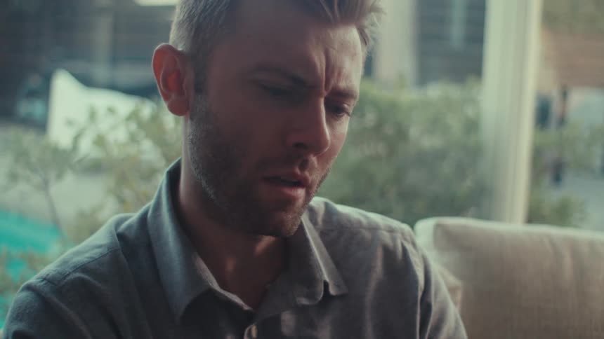 Male sitting indoors on a couch and is talking to someone