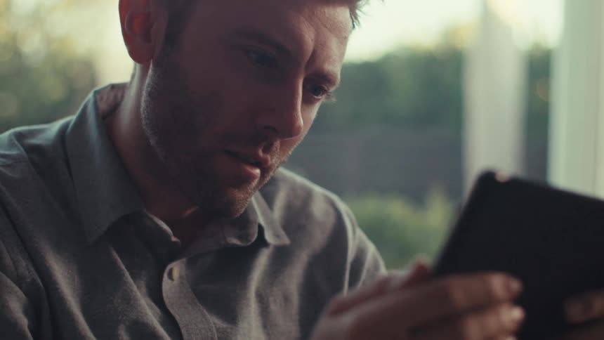 A man sitting at home holds a smartphone in his hands