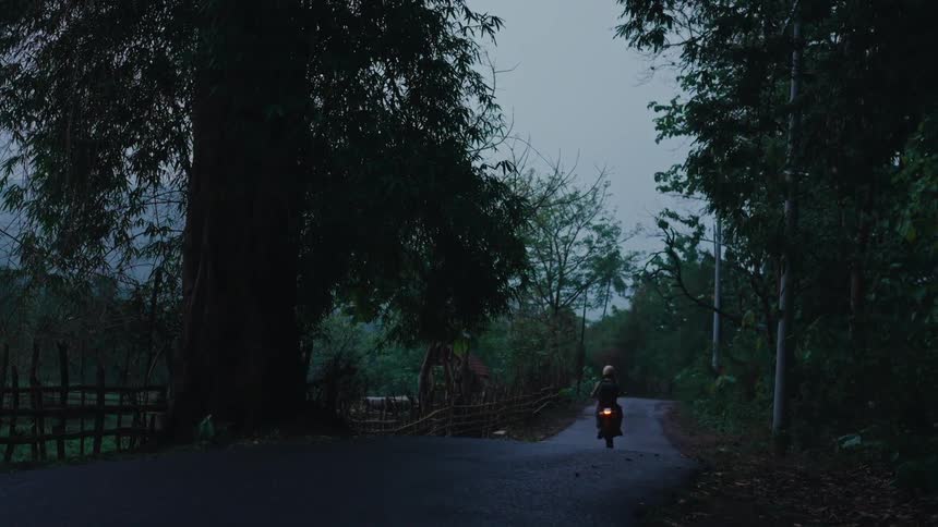 In a wooded rural area a man is driving his motorcycle