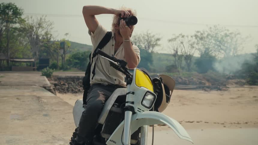 Man sitting on a motorcycle as he holds his camera and takes pictures