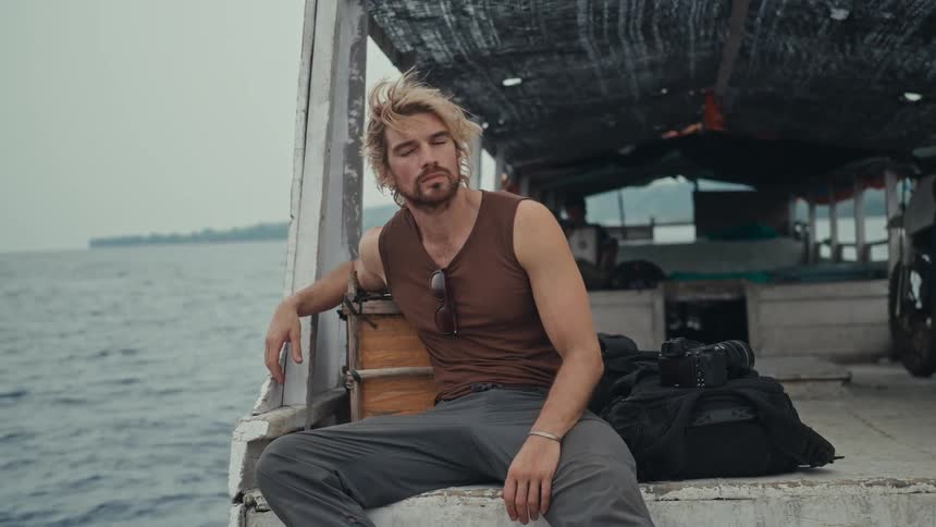 Man sitting on the back of a boat as it sails off the coast