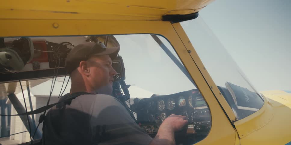 A pilot is seated in the cockpit of a yellow aircraft operates the controls and instruments starts engine