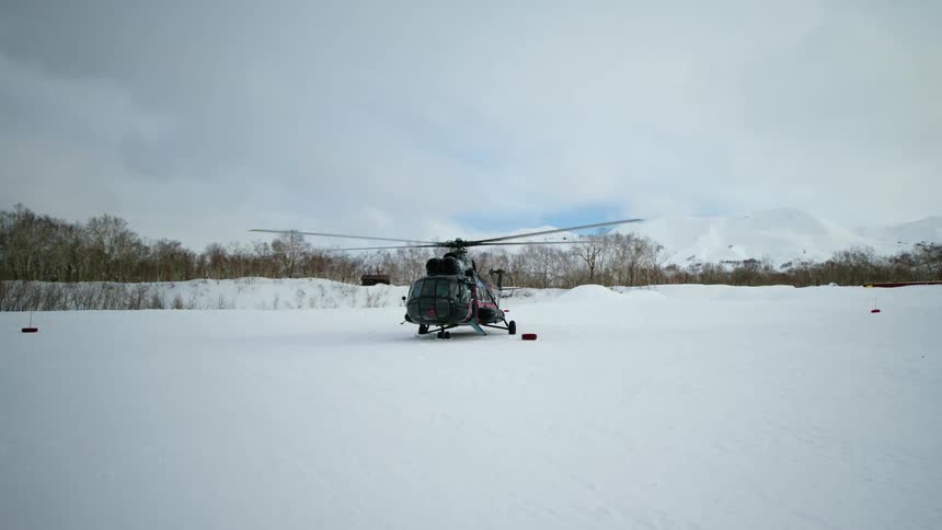 A military helicopter sits on a snowy airfield ready for takeoff