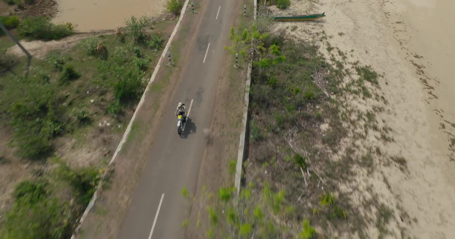Aerial view of a motorcycle traveling along a narrow highway with sparse vegetation