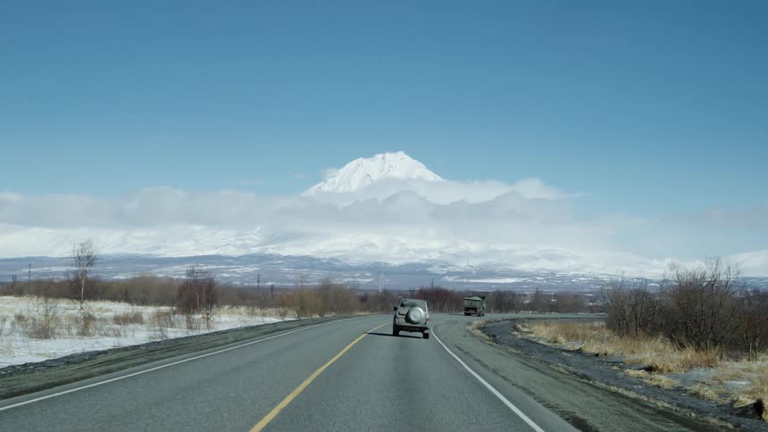 Cars drive along a road with a mountain in the distance