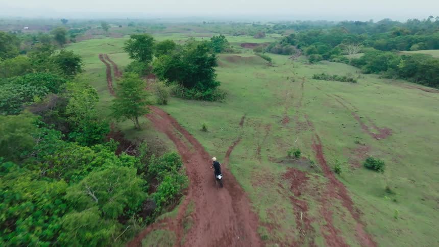 A rider on a motorbike traversing a winding dirt road through a lush green landscape