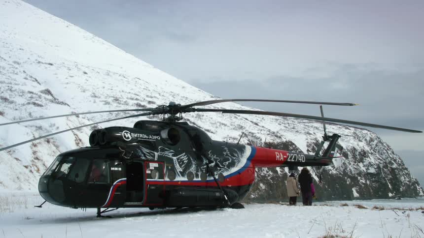 A helicopter is parked on a snowy landscape with mountains in the background