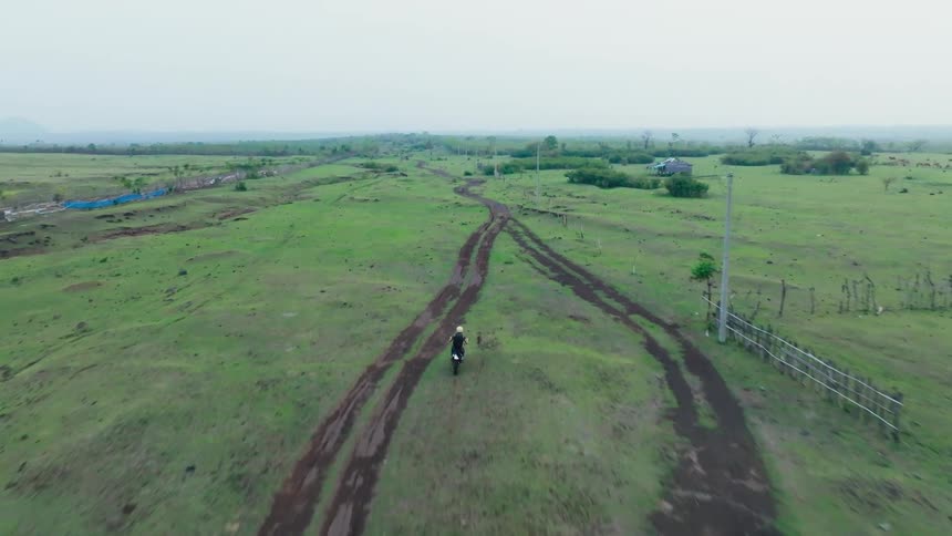 A motorcyclist riding along a dirt road through a vast open field