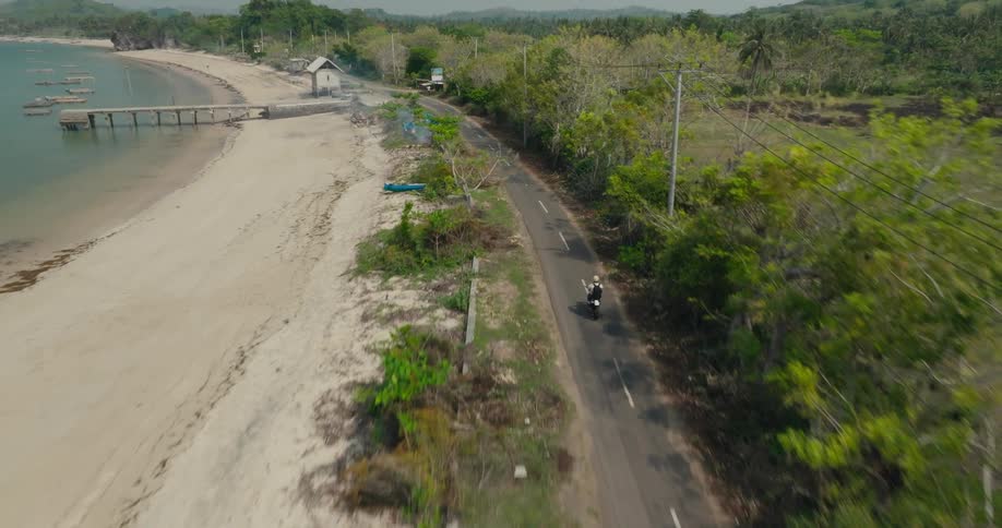 Person is riding a motorcycle on a road by the coast of a beach