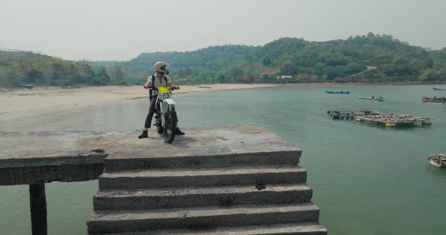 Person in helmet riding a motorcycle on a concrete pier in the sea