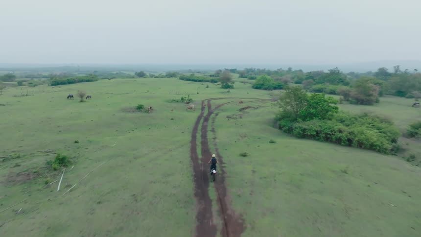 A man wearing a helmet rides a dirtbike on a dirt road that winds through a grassy landscape