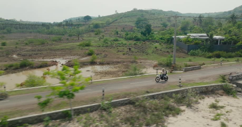 Aerial view of a person traveling on a motorcycle on a highway surrounded by mountains and vegetation