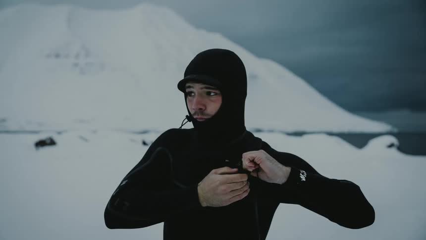 A person in a black wetsuit is adjusting the zipper in a snowy mountainous landscape