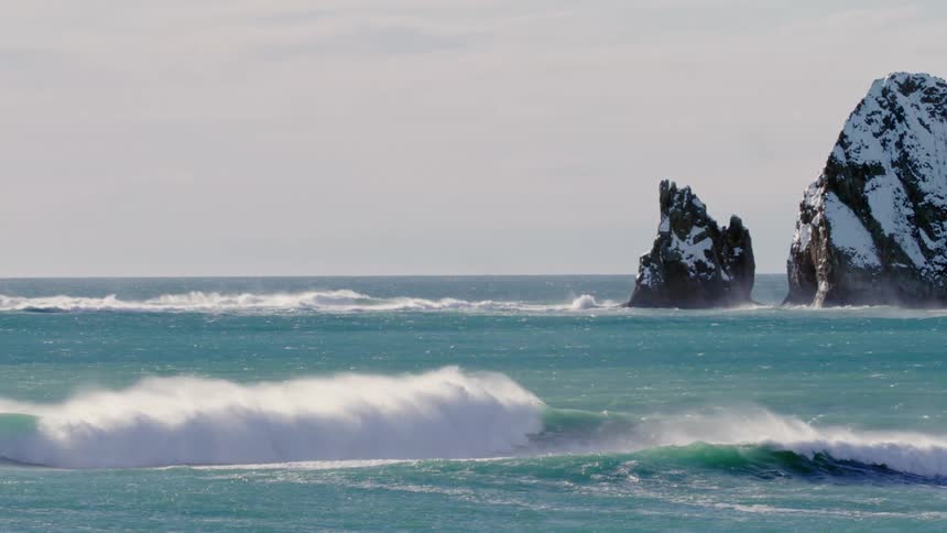 A large ocean with some waves breaking near the shore and there are some huge rocks in the water