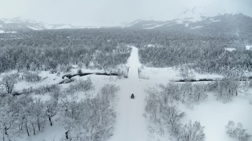 A desolate winter landscape with a snowcovered road winding through a vast snowy forest with a black car driving along it