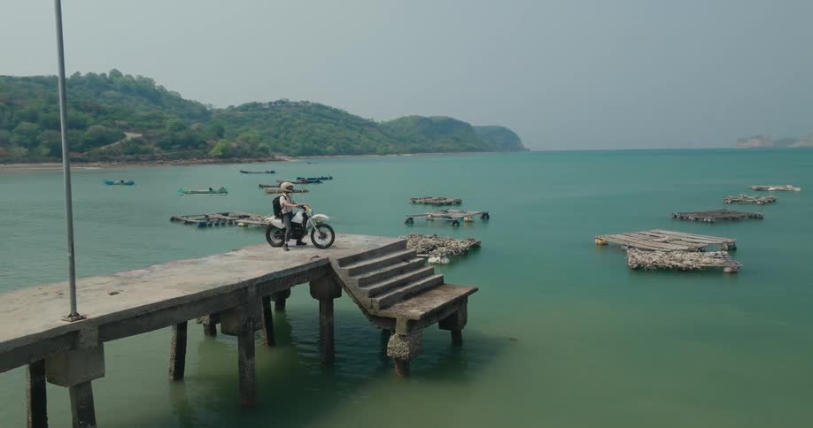 Man in helmet sitting on a motorcycle on a concrete pier by the sea