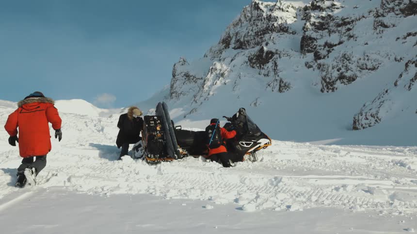 People trying to flip over a crashed snowmobile in the mountains