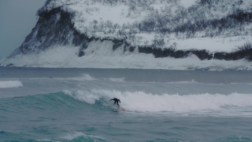 A man is surfing near the snow covered shore