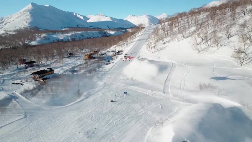 A red helicopter takes of from a snowcovered mountainside nestled amongst a picturesque winter landscape
