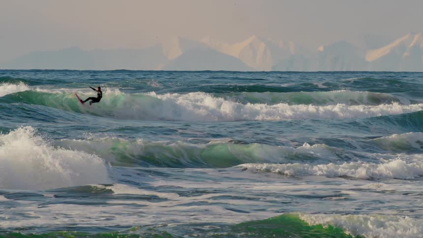Surfer riding waves in an ocean with snowy mountains on the horizon