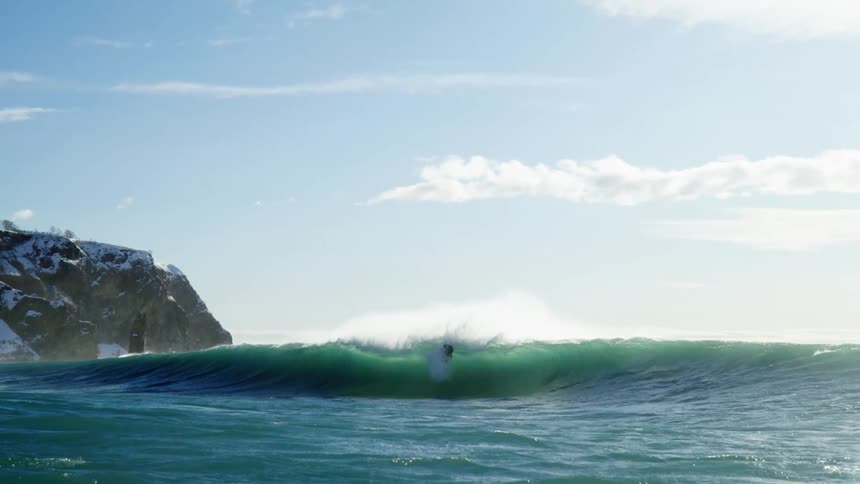 Surfers in wetsuits riding large waves in a cold snowy landscape