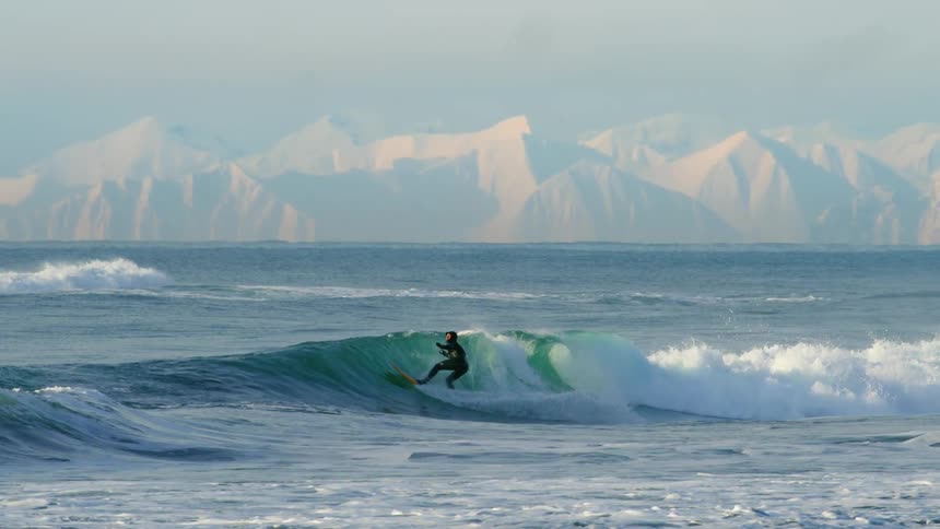Person is surfing in the arctic ocean near glaciers in winter