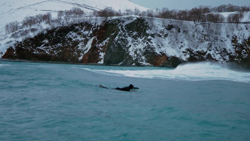 Surfer swimming on surfboard in the sea with snowy mountains in the background
