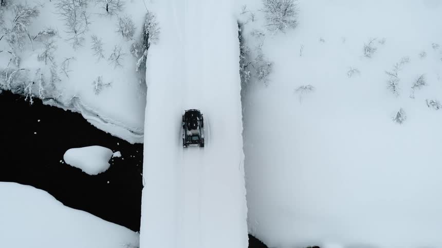Truck traveling on a snow covered bridge over a stream on a winter day