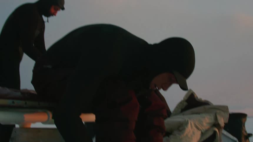 Two men putting on clothes and boots while standing in a completely snowy environment