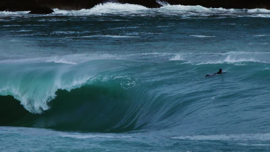 Surfer waits for a perfect wave amidst the deep blue waters of the ocean as a powerful wave begins to form