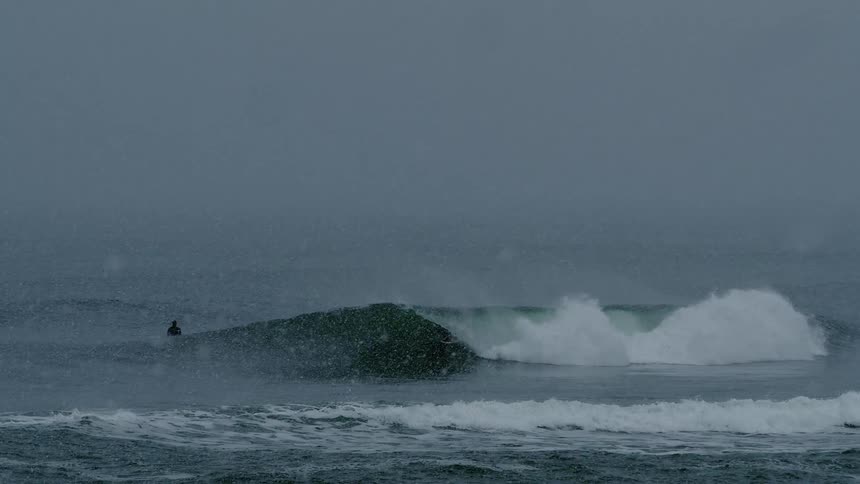A surfer riding a powerful wave in the ocean with snow falling in the foreground