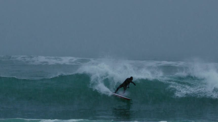 A person wearing a black wetsuit is surfing a wave and doing some tricks