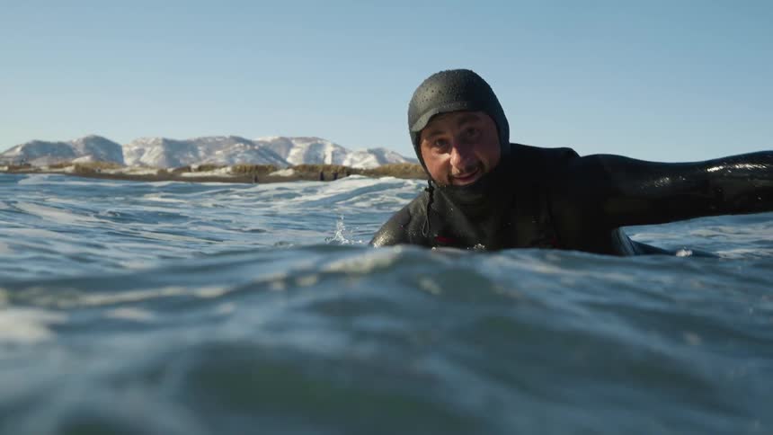 A man smiles as he paddles out into the water on his surf board