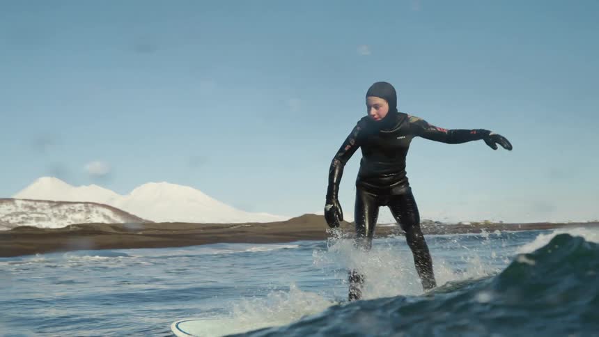 Surfer wearing a wetsuit balances on his surfboard as he rides a wave